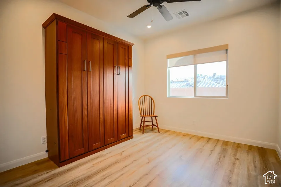 Built-in wood-finish cabinetry, wood-finish flooring, ceiling fan with integrated lighting, and a window with roller shade