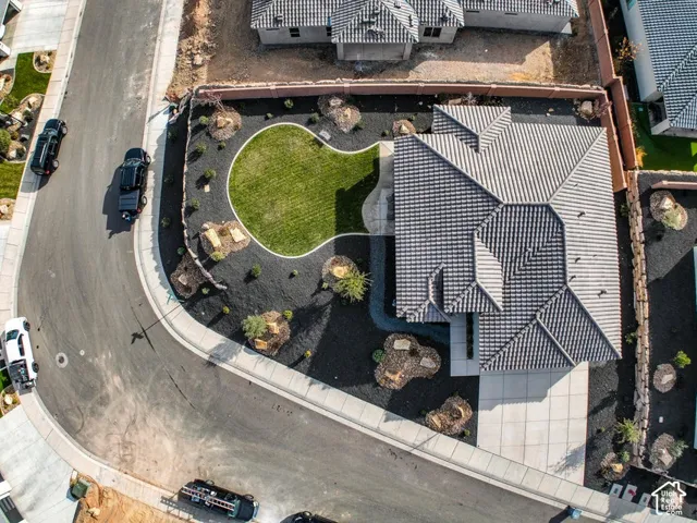 Pitched tile roof with multiple gables, extensive dark rock landscaping, manicured lawn feature, concrete driveway, and concrete sidewalk