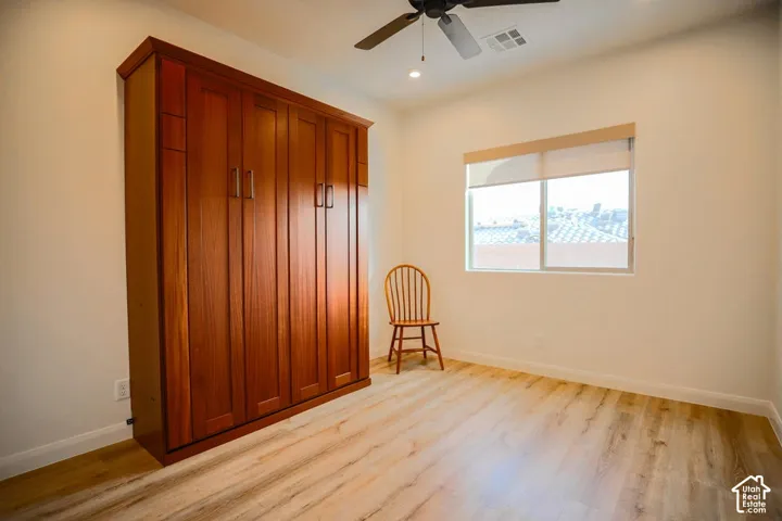 Built-in wood-finish cabinetry, wood-finish flooring, ceiling fan with integrated lighting, and a window with roller shade