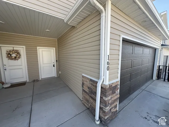 Brown paneled garage door, beige horizontal siding, and a stacked stone accent