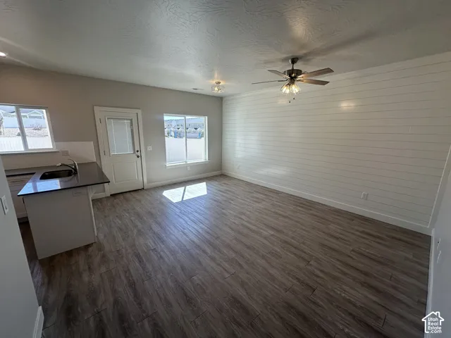 Wood-finish flooring, white shiplap accent wall, dark countertops, ceiling fan with integrated lighting, and multiple windows