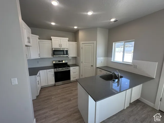 Modern kitchen featuring white cabinetry, stainless steel appliances, dark countertops, a white subway tile backsplash, and wood-finish flooring