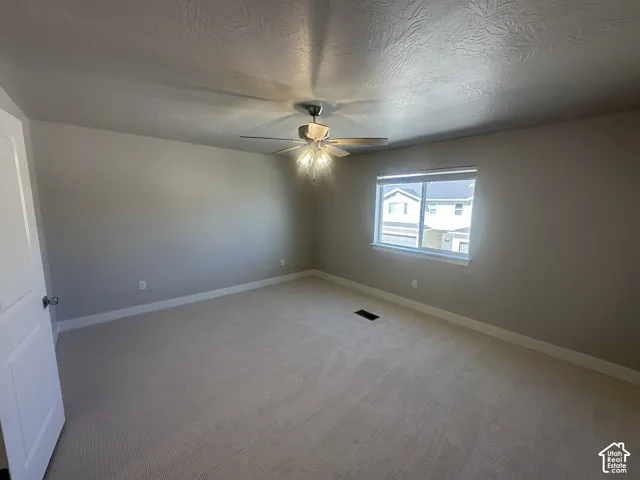 Neutral tone wall paint, light-colored carpeting, window with blinds, and ceiling fan with integrated lighting