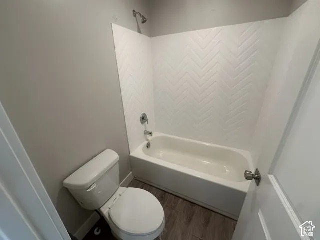 Bathtub with chevron-patterned tile surround, polished chrome fixtures, and wood-finish flooring