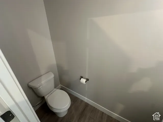 Wood-finish flooring with white baseboards, a white toilet, and a wall-mounted toilet paper holder