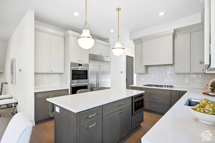 Contemporary kitchen featuring a large central island, white countertops, built-in stainless steel appliances, and a tiled backsplash