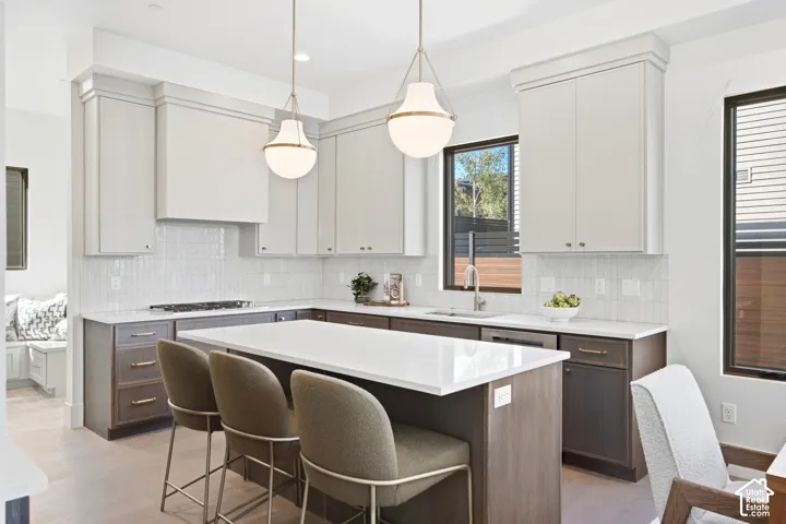 Modern kitchen featuring white shaker upper cabinetry and dark wood-finish lower cabinetry, a center island with seating, a gas range, and a tile backsplash
