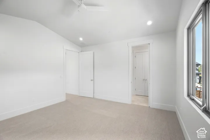 Neutral tone carpeting, recessed lighting, ceiling fan, white paneled doors, and a large window with dark trim