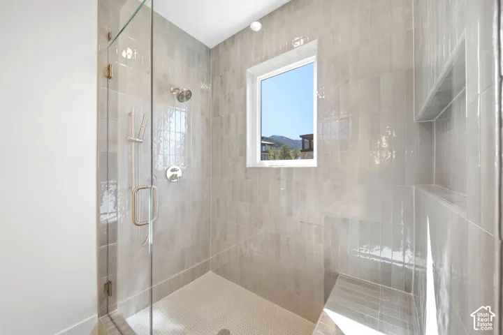 Glass-enclosed shower with a rainfall showerhead, handheld shower, integrated tiled bench, and recessed shelving