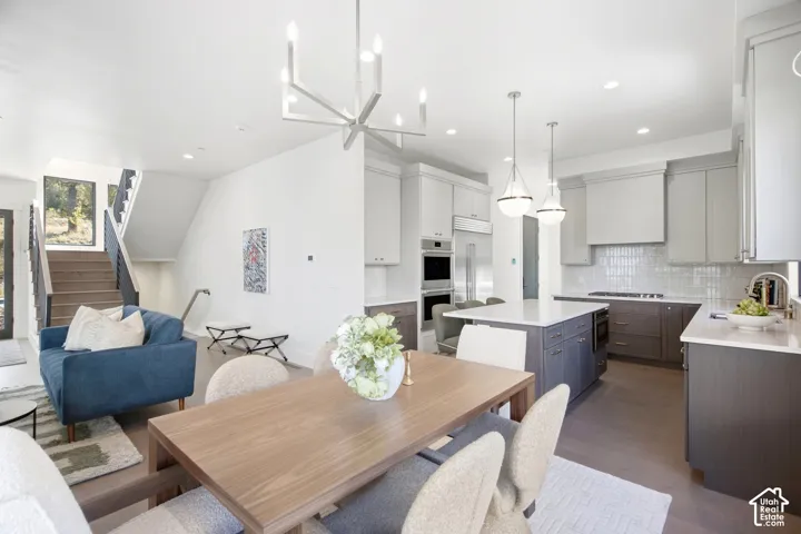 Open-concept living space featuring wood-finish flooring, a modern chandelier, and a built-in kitchen with an island, integrated appliances, and pendant lighting