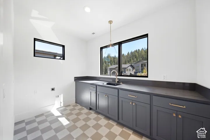 Laundry area featuring a checkered tile floor, dark grey cabinetry with brass hardware, and a single basin sink with a gold-tone faucet