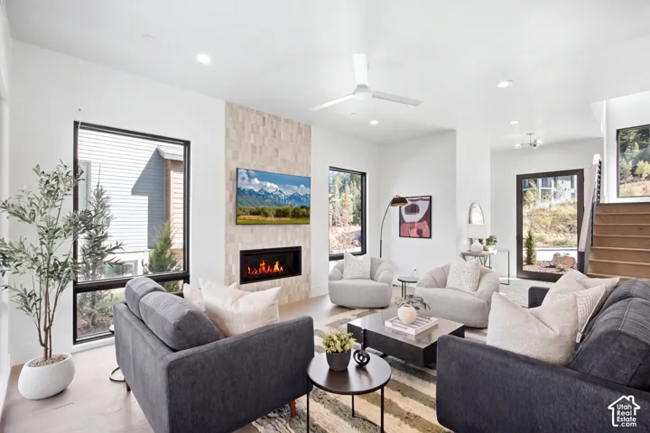 Open-concept living space featuring wood-finish flooring, a contemporary fireplace with a tiled surround, recessed lighting, and a modern ceiling fan