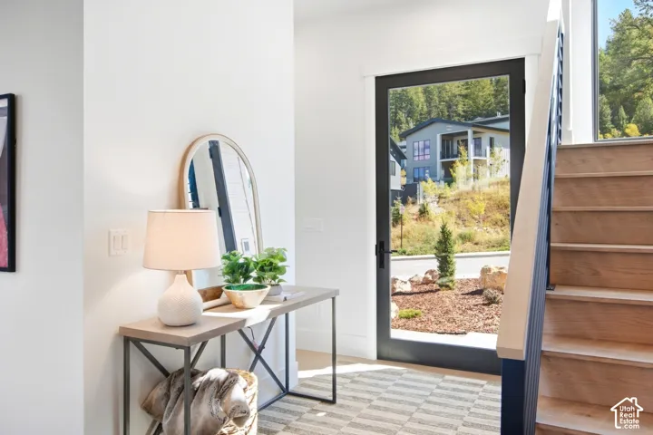 Black-framed glass entry door, wood-finish staircase with dark balusters, white wall finishes, and a neutral patterned area rug