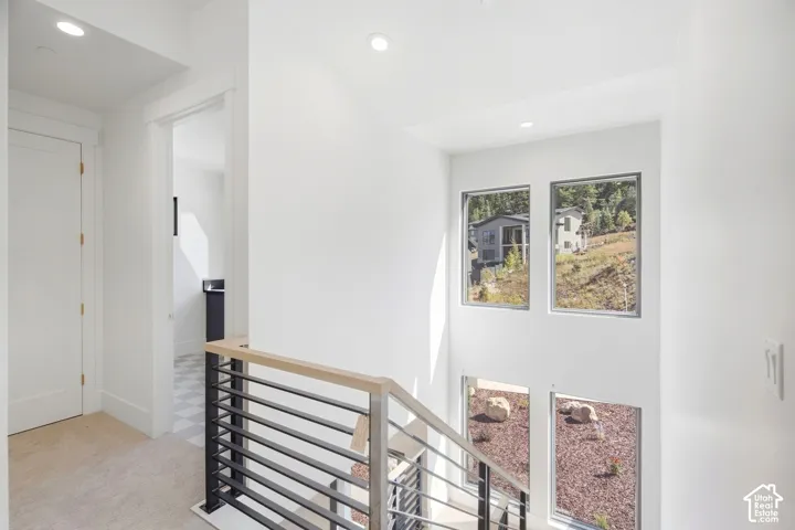 Modern staircase featuring a stainless steel and wood handrail, multiple windows, recessed lighting, and white walls