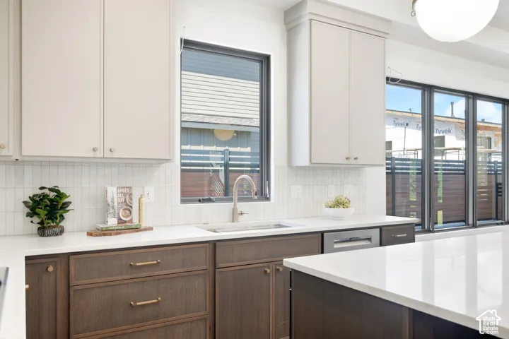 White countertops with integrated sink, dual-toned cabinetry, vertical tile backsplash, and dark-framed windows