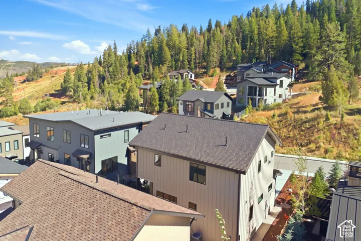 New construction residences with pitched and flat roofs, and a natural forested hillside backdrop