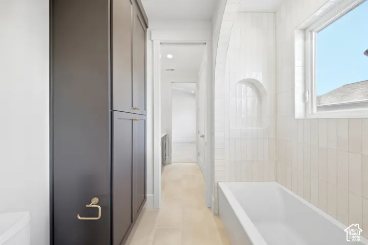 Built-in dark cabinetry, recessed lighting, tiled flooring, white subway tile wall surround, and a built-in tub with an arched tiled niche