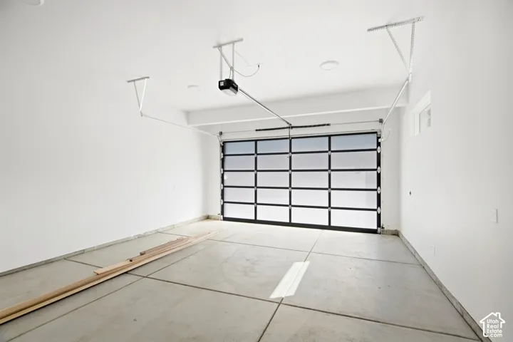 Spacious garage featuring a modern glass panel garage door, concrete flooring, recessed lighting, and a garage door opener