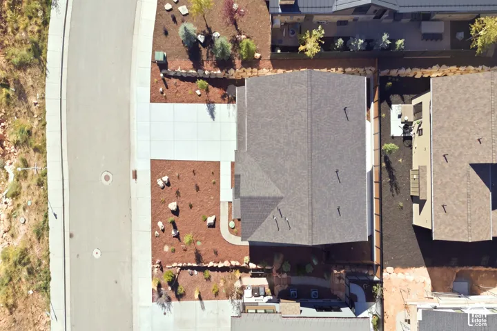 Asphalt shingle roofing, paved driveway, concrete walkways, xeriscaping with decorative rocks, and a stone retaining wall