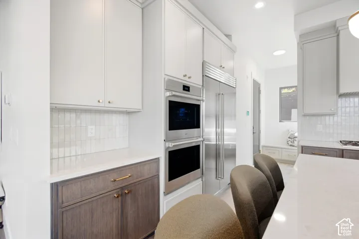 Stainless steel appliances, built-in double oven, paneled refrigerator, white shaker-style cabinetry, and a subway tile backsplash