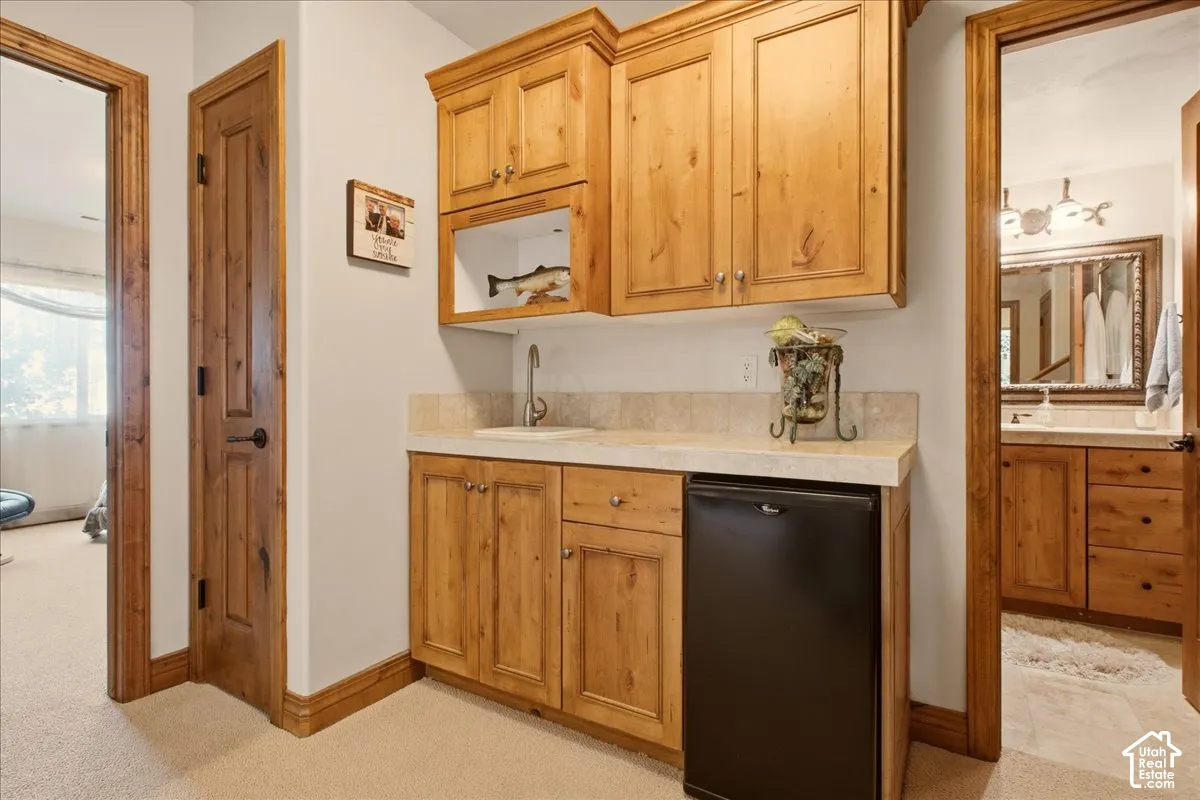 Wet bar featuring wood-finish cabinetry, a built-in sink, and an integrated compact refrigerator
