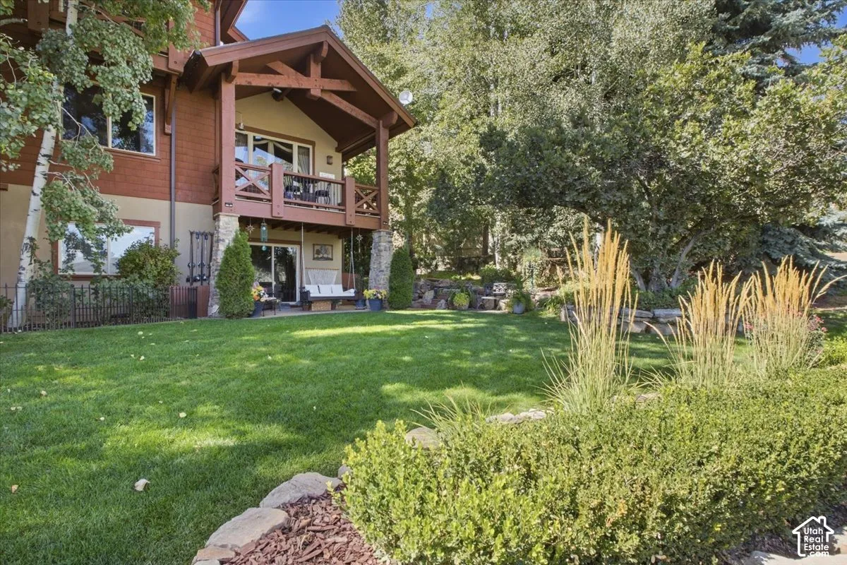 Expansive green lawn with established landscaping, a multi-level deck, and a lower patio with sliding glass doors