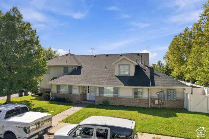 Multi-level building with dormer windows, a dark shingled roof, a paved walkway, and a landscaped lawn