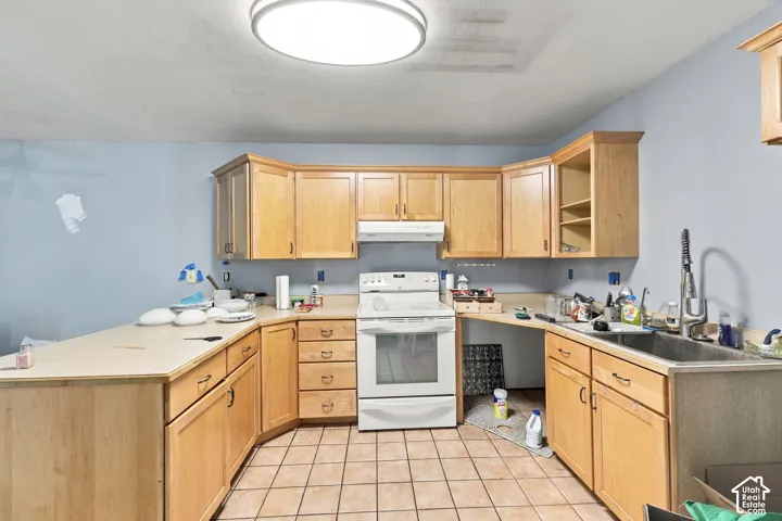 U-shaped kitchen layout featuring light wood-finish cabinetry, tile flooring, and a white range