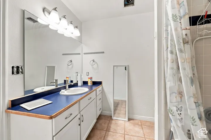 Extended vanity with a single sink, large wall-mounted mirror, and tile flooring