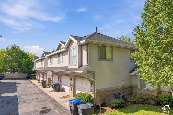 Multi-story property featuring stucco and brick exterior, individual garage doors, and shingle roofing