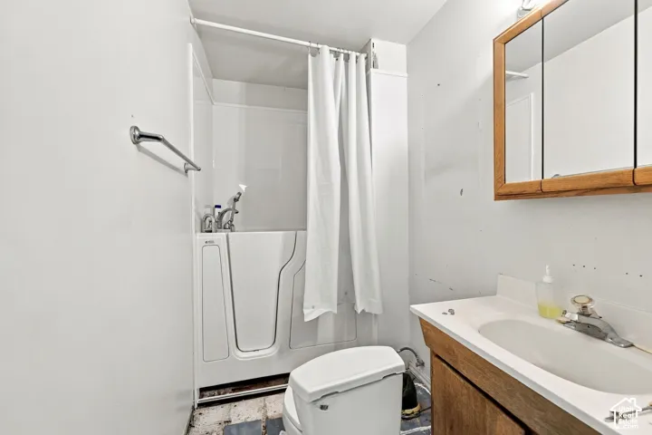 Walk-in bathtub with shower curtain, wood-finish vanity with countertop sink, and mirrored medicine cabinet