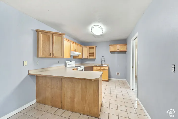 U-shaped kitchen featuring wood cabinetry, light-toned countertops, and tile flooring