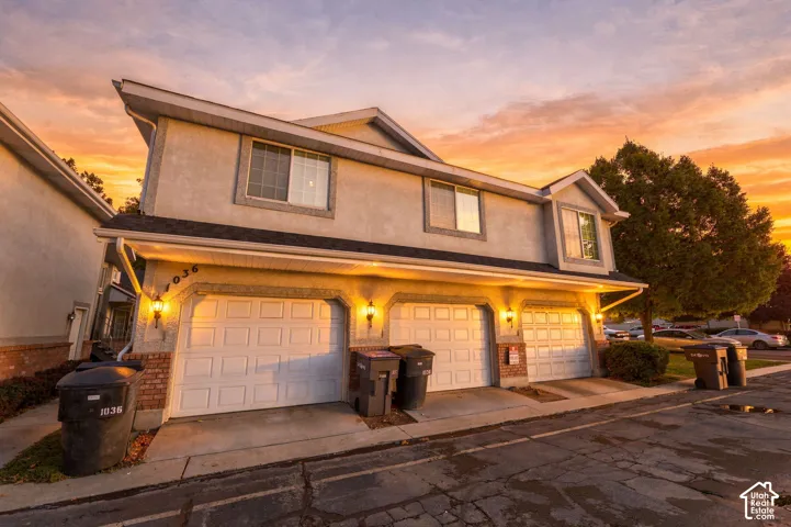 Stucco exterior with multiple white garage doors, exterior wall sconces, and brick accents