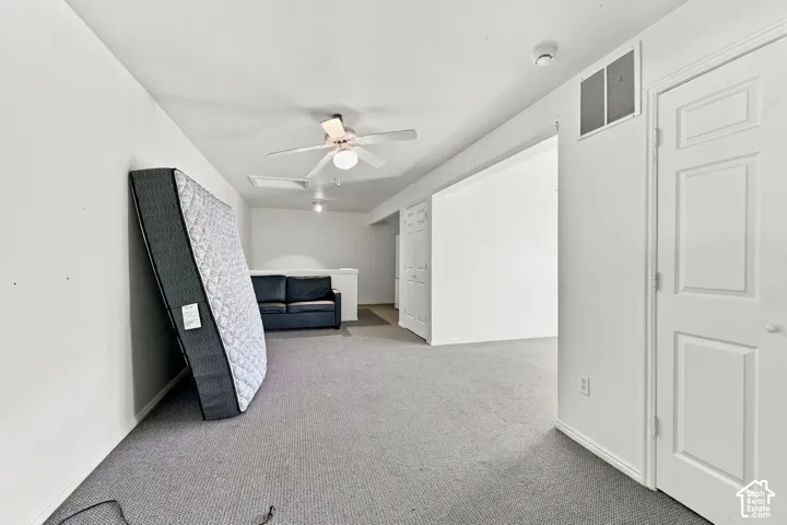 Carpeted room with a ceiling fan, white paneled doors, and white walls