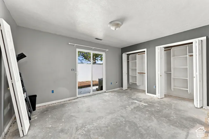 Sliding glass door, two bi-fold door closets, built-in closet shelving, overhead flush mount lighting, and grey painted walls