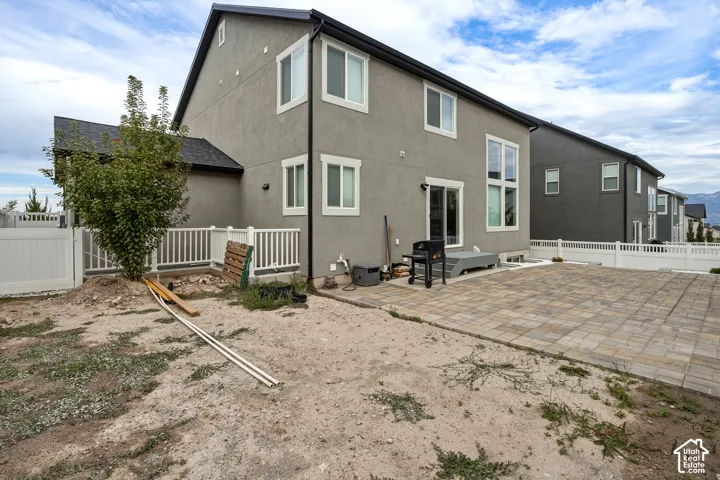Rear exterior featuring stucco siding, multiple windows, a sliding glass door, a white privacy fence, and a paver patio