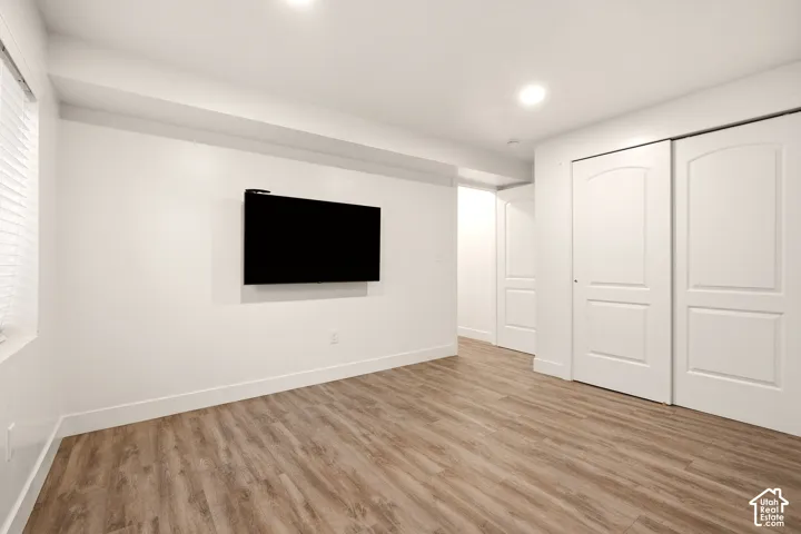 Recessed lighting illuminates the space, featuring wood-finish flooring, a wall-mounted television, and white sliding closet doors with arched paneling