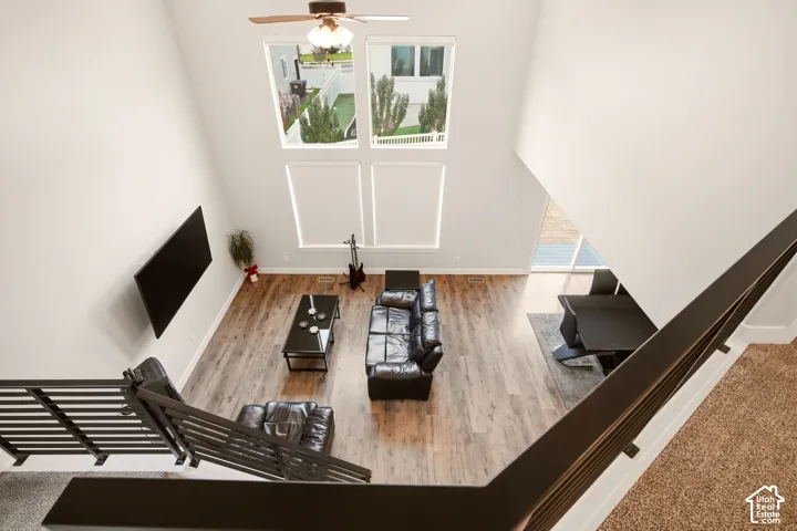 Two-story living area featuring wood-finish flooring, a ceiling fan, and multiple windows