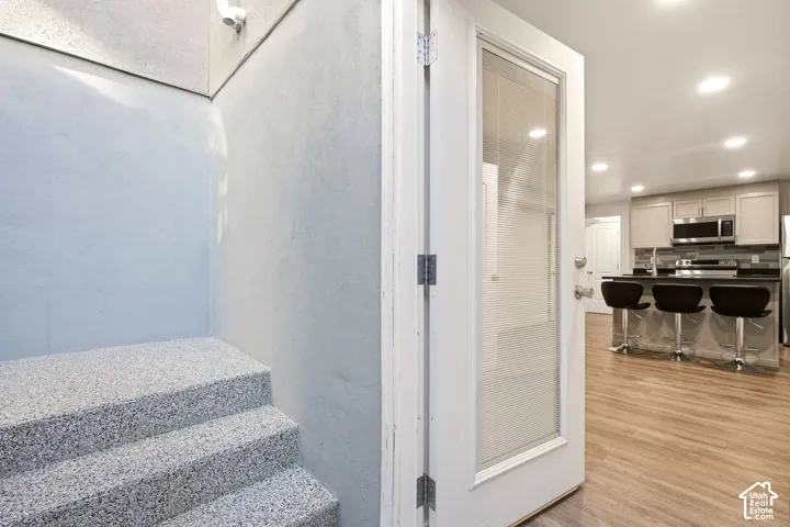 Wood-finish flooring, recessed lighting, and a kitchen featuring a center island with bar seating, stainless steel appliances, and a tile backsplash