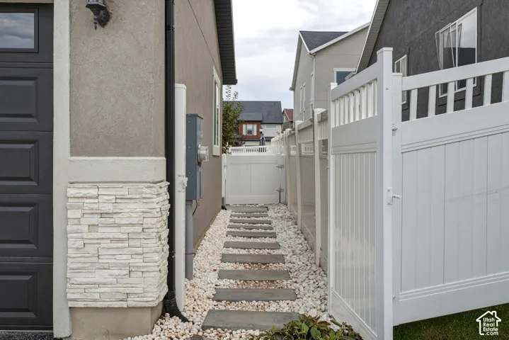Stucco exterior with stacked stone accents, dark panel garage door, white picket fence, white gravel, and stepping stone pathway