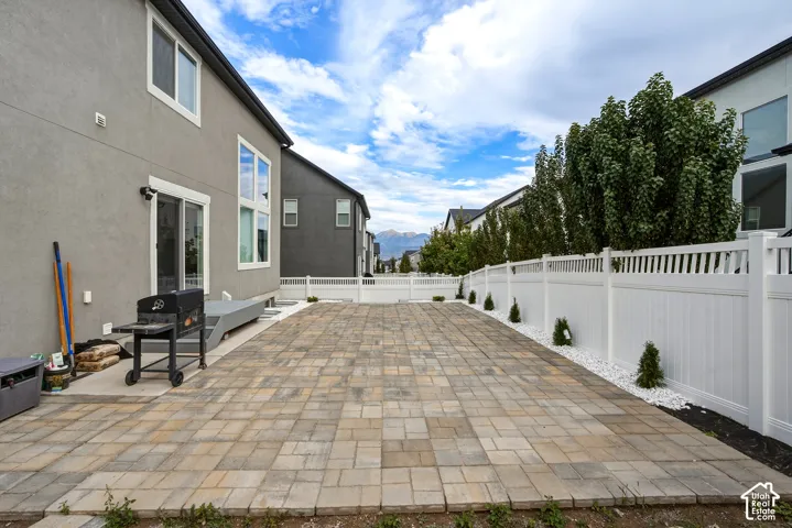 Paved patio area, white privacy fencing, and mature trees