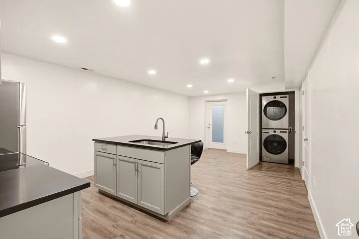 Open-concept living space with recessed lighting, wood-finish flooring, and a kitchen island featuring a stainless steel sink and matte black faucet