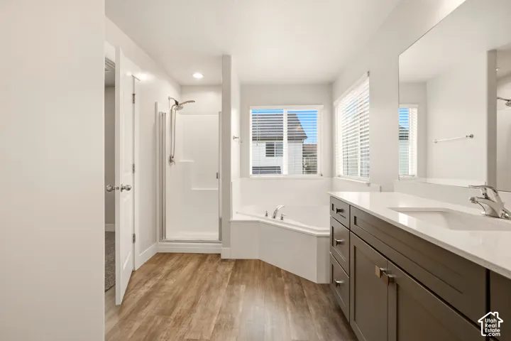 Spacious bathroom featuring a dual vanity with a light-toned countertop, a corner soaking tub, a stand-alone shower, and wood-finish flooring