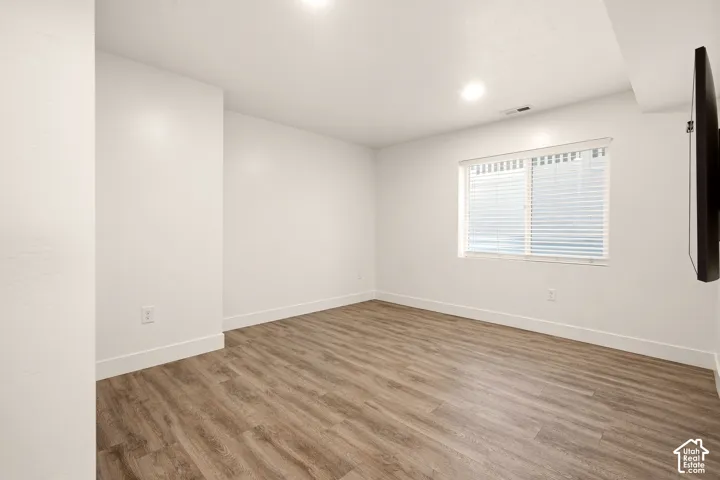 Recessed ceiling lighting, wood-finish flooring, white walls, and a window with blinds