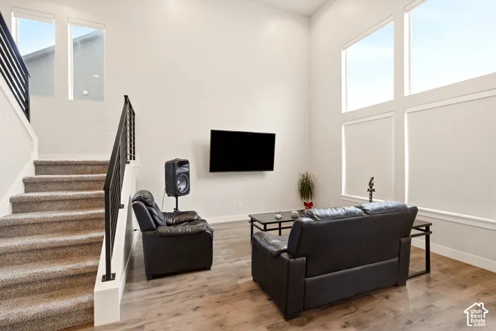 Vaulted ceiling with high windows, wood-finish flooring, carpeted staircase, and contemporary black metal railing