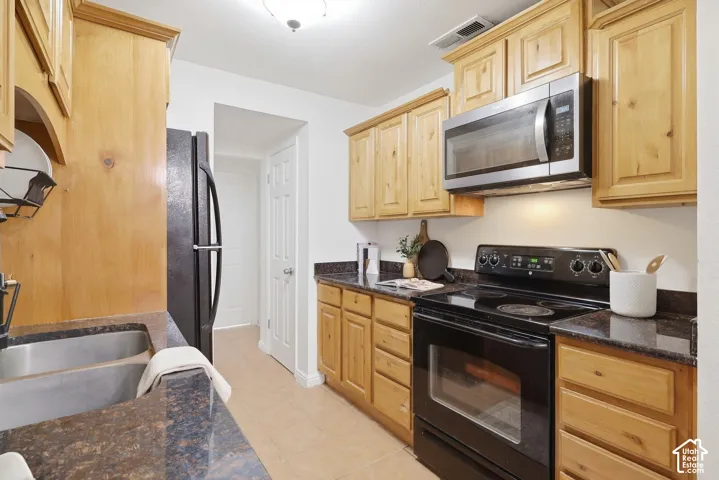 Kitchen featuring wood cabinetry, dark countertops, a stainless steel microwave, black electric range, and a double basin sink