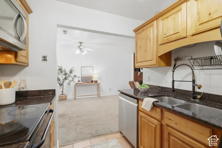 Wood-finish cabinetry, stainless steel microwave, black electric stovetop, double basin sink, and wood-finish flooring