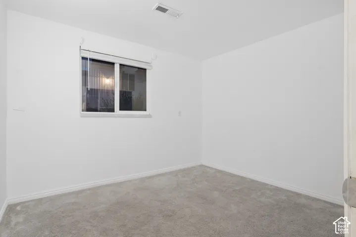 White painted walls with a single window featuring blinds, complemented by grey carpeting and white baseboards