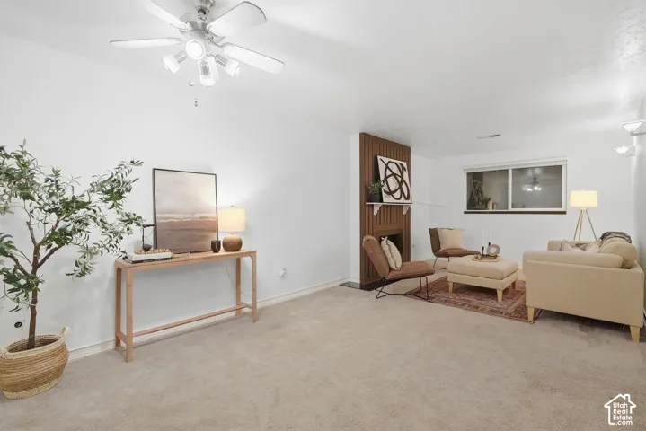 Carpeted living space featuring a fireplace with wood paneling, a ceiling fan with integrated lighting, and a window