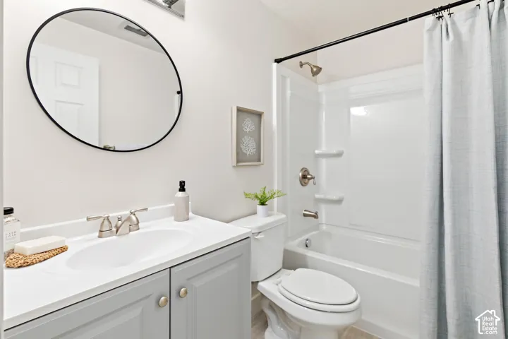 Bathroom featuring a single vanity with light grey cabinetry, a round mirror, and a white tub with an integrated shower